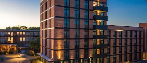 A modern multi-story building with a brick facade, large windows, and outdoor seating areas.
