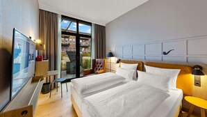 Habitación de hotel con dos camas, televisión, escritorio y vista a la ciudad.