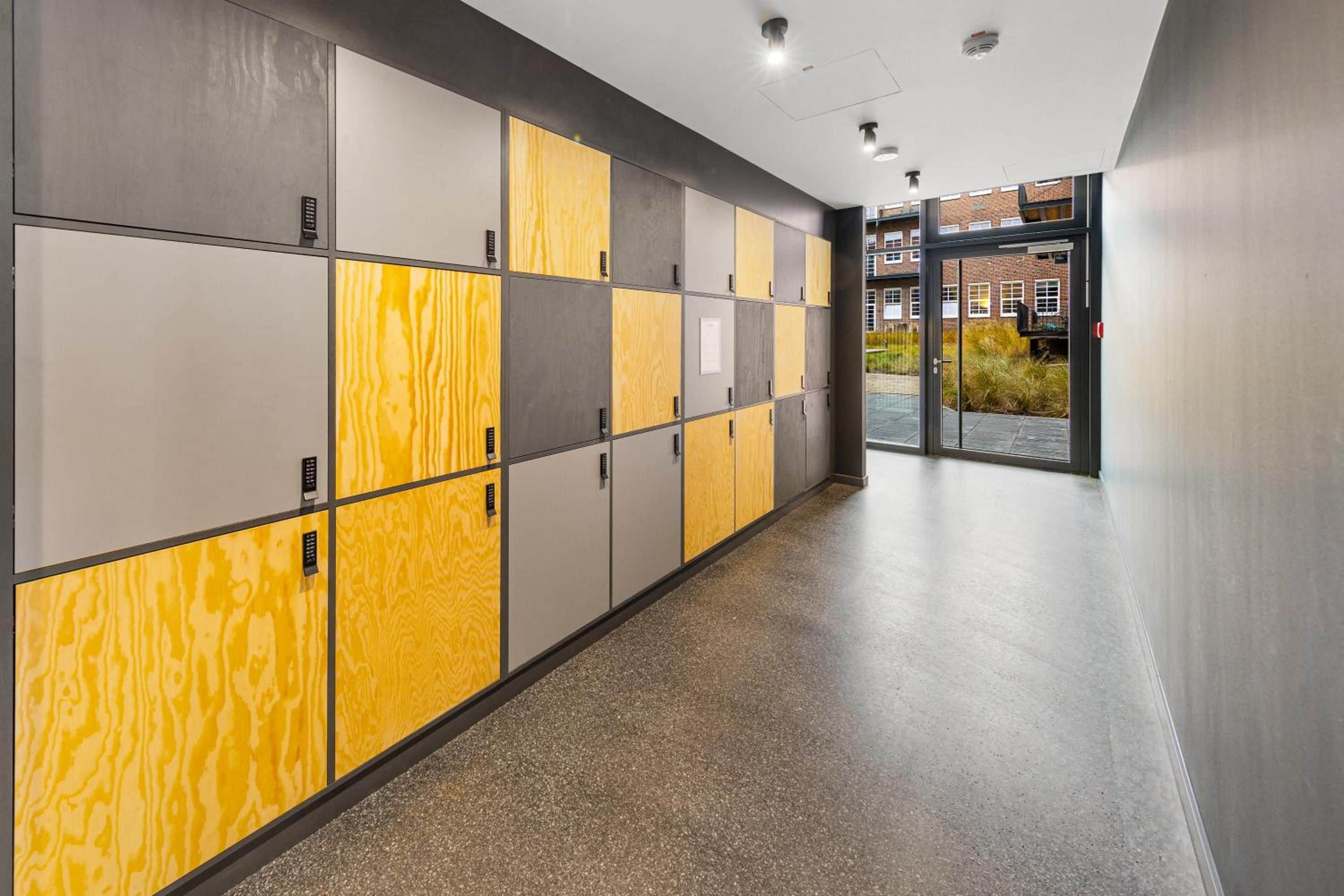 A hallway with lockers, a glass door entrance, and a view of a building with windows.