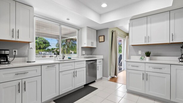 Una cocina moderna con armarios blancos, lavavajillas y ventana con persianas.