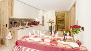 A modern kitchen with a dining area set for a meal, featuring a striped tablecloth, red and white plates, and a vase of red roses. - Apartment Véronique, front of village location (Montgenevre)