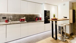 A modern kitchen with white cabinets, a marble backsplash, a coffee machine, and a small table with stools. - Apartment Véronique, front of village location (Montgenevre)