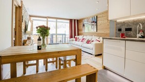A modern kitchen with white cabinets, a wooden dining table, and a large window. - Apartment Véronique, front of village location (Montgenevre)