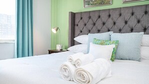 A neatly made bed with rolled white towels, a grey tufted headboard, and patterned pillows. - Upgraded Historic Condo in Atlanta (Atlanta)