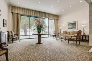 Una habitación amplia con un ventanal grande, una mesa redonda con un florero, un sofá y dos sillones.