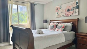 A neatly made bed with pillows and a folded towel, a bedside table, a lamp, and a floral artwork on the wall. - Downtown Atlanta Condo with City View (Atlanta)