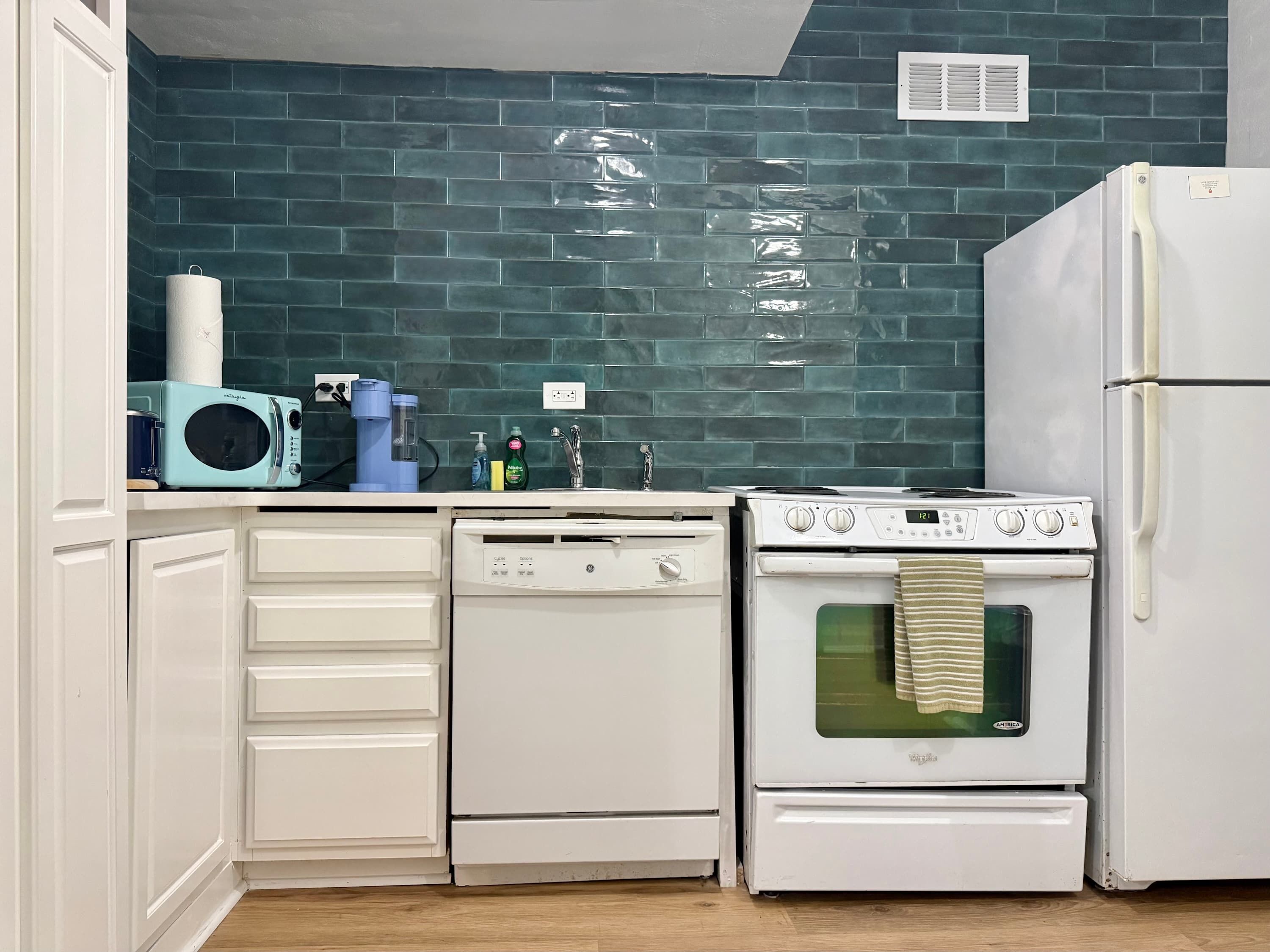 Une cuisine avec des meubles blancs, un micro-ondes bleu, une cuisinière blanche et un réfrigérateur blanc.