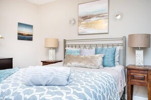 Une chambre à coucher comprenant un lit, deux tables de chevet, une petite table d’appoint, une lampe fixée au mur et deux œuvres d’art murales.