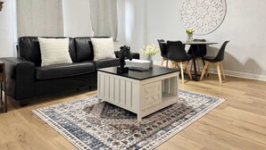 A modern living room with a black leather sofa, a white coffee table, a dining table with chairs, a ceiling fan, and a decorative wall piece. - Condo in the Heart Atlanta w/ Private Balcony (Atlanta)