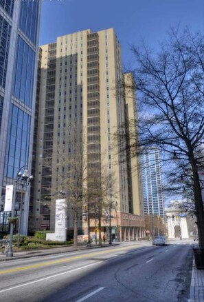 A tall building with a modern glass facade, a clear sky, and a street with a few trees. - Condo in the Heart Atlanta w/ Private Balcony (Atlanta)