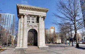 A classical stone archway with inscriptions, surrounded by a paved plaza and leafless trees, with modern buildings in the background. - Condo in the Heart Atlanta w/ Private Balcony (Atlanta)