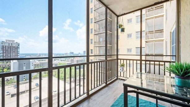 A balcony with a clear view of the cityscape, a potted plant, and a glass table.