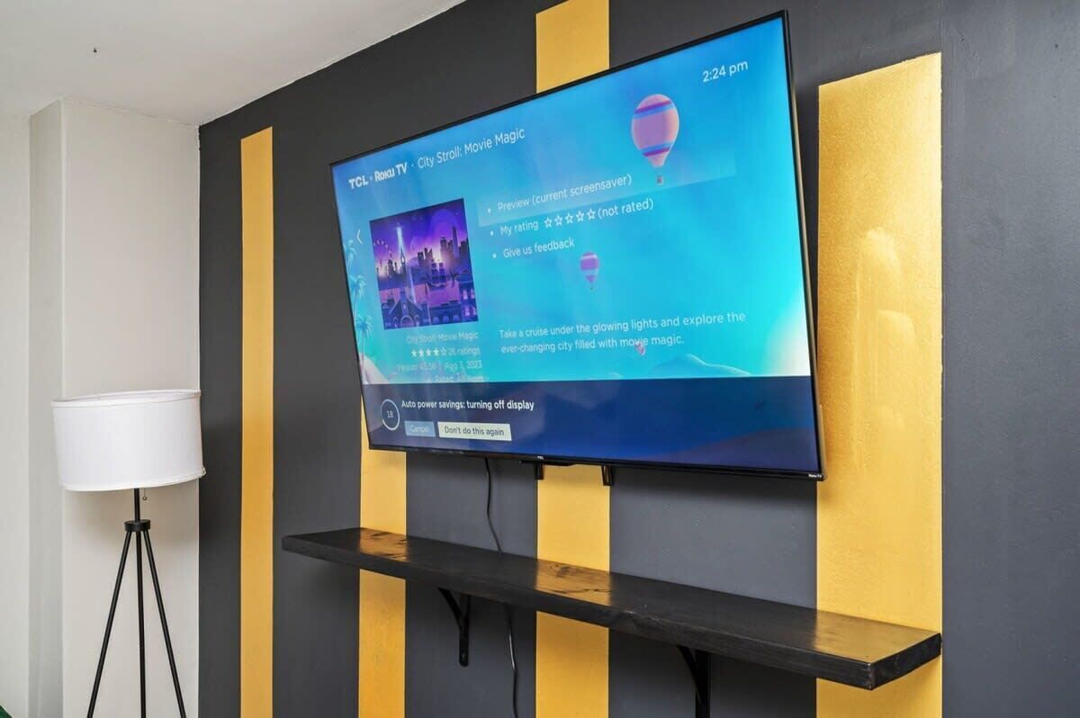Ein Flachbildfernseher an einer Wand mit gelb-schwarz gestreiftem Muster, der einen Filmplakat für "City Stroll: Movie Magic" zeigt.