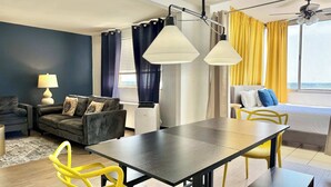 A modern living room with a dark sofa set, a dining table with yellow chairs, and a ceiling fan. - Stunning 22nd-Floor Condo with City Views (Atlanta)