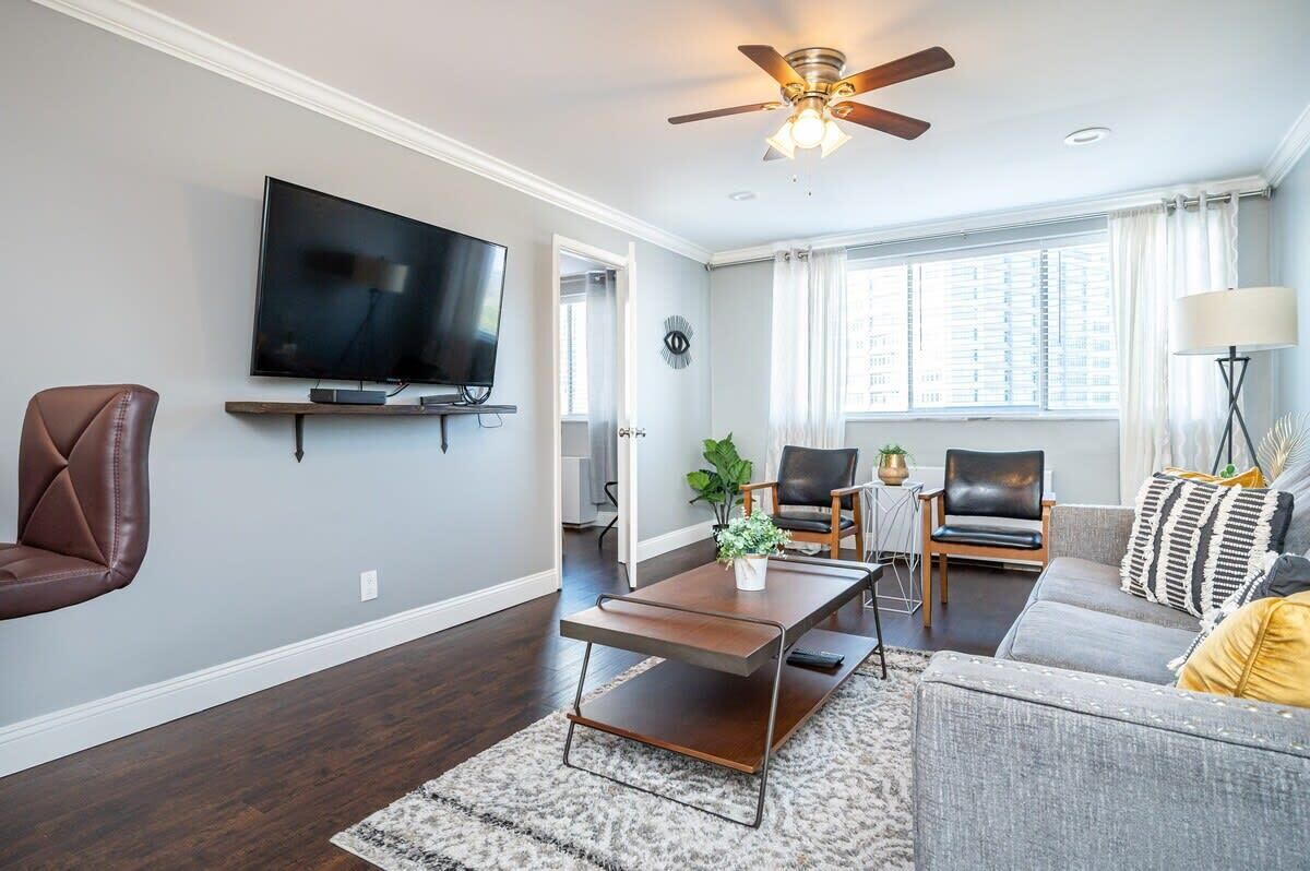 A modern living room with a flat-screen TV, a ceiling fan, and a sofa.
