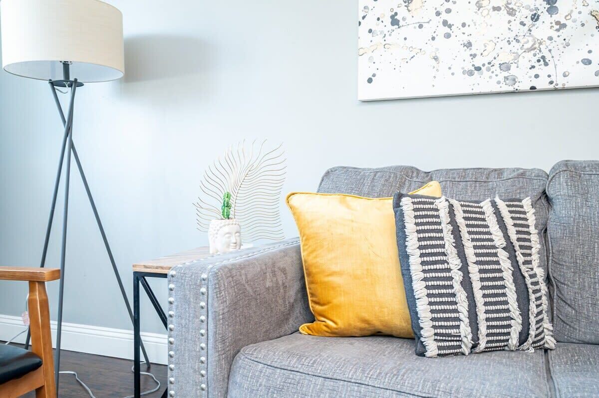 A grey sofa with two cushions, a small table with a plant, and a floor lamp.