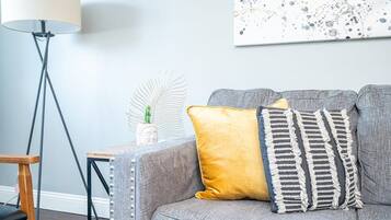A grey sofa with two cushions, a small table with a plant, and a floor lamp.