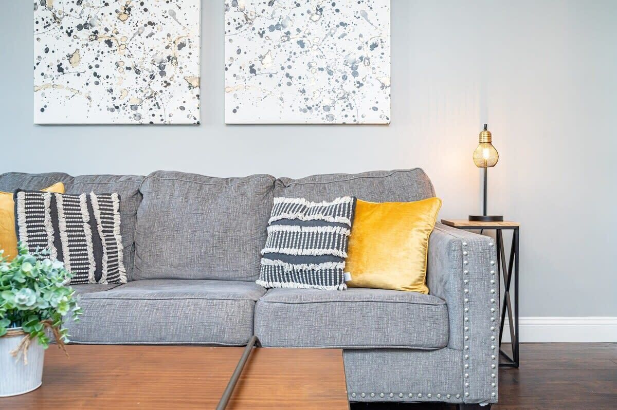 A gray sectional sofa with patterned cushions, a small side table with a lamp, and a plant on a wooden floor.