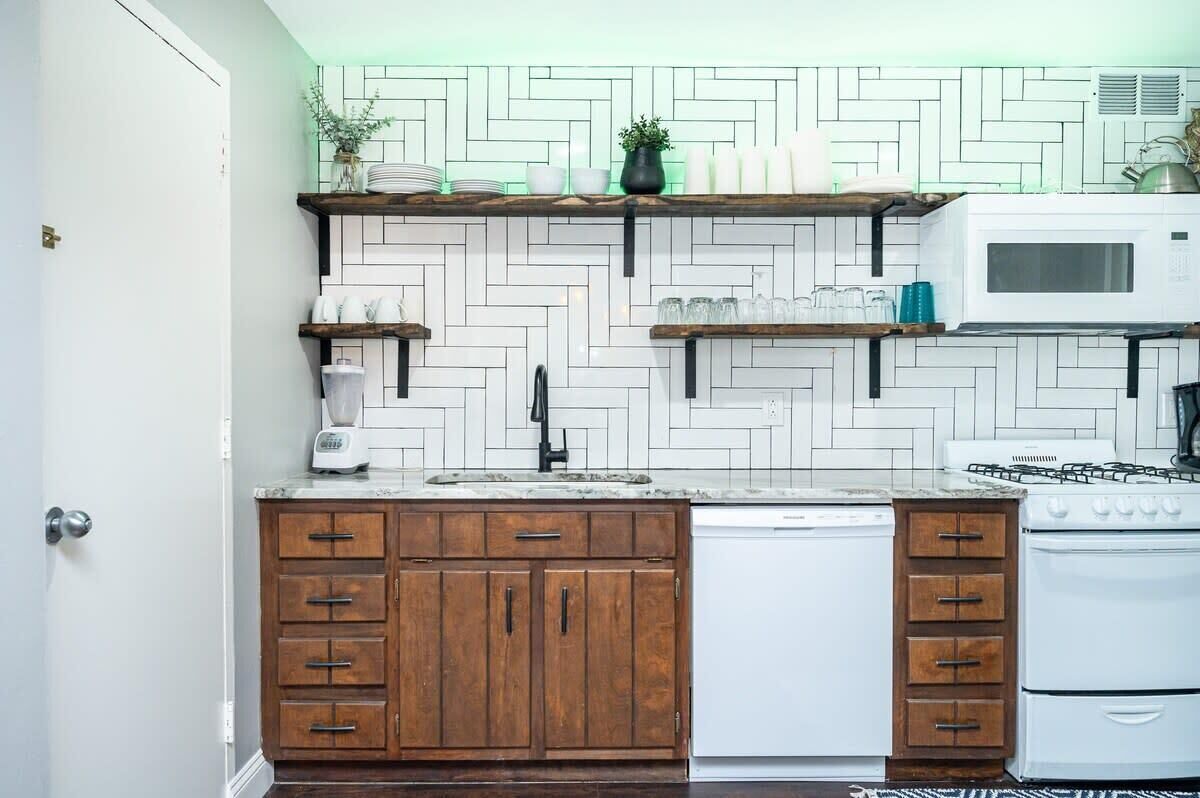 Une cuisine avec un dosseret en carreaux de céramique blancs disposés en motif chevrons, des armoires en bois, un lave-vaisselle blanc et une cuisinière.