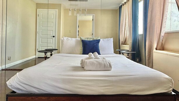 A hotel room with a large bed, bedside tables, a mirror, and curtains. - Upgraded 2BR Condo Near ATL Attractions (Atlanta)