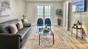 Ein modernes Wohnzimmer mit einem Ledersofa, zwei blauen Sesseln, einem Glastisch, einem großen Flachbildfernseher und einem Blumentopf.