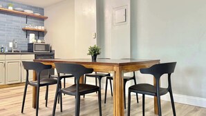 Ein Essbereich mit einem Holztisch und vier schwarzen Stühlen. Im Hintergrund ist eine Küche mit einer Mikrowelle und einem Spülbecken zu sehen.