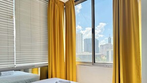 A hotel room with a large window, yellow curtains, and a neatly made bed with white linens. - Downtown Atlanta Condo with City View (Atlanta)