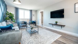 Una sala de estar moderna con un sofá, un sillón, una mesa de centro y un televisor montado en la pared.