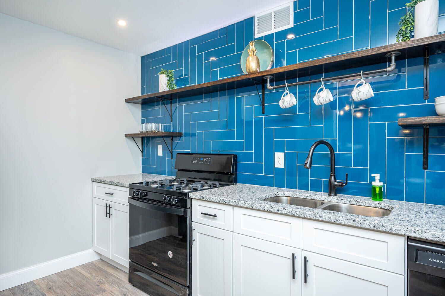 A kitchen with blue tiled backsplash, white cabinets, a black stove, and a stainless steel sink.