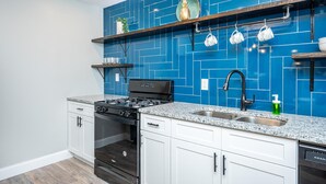 Una cocina con salpicadero de azulejos azules, armarios blancos, una estufa negra y un lavabo de acero inoxidable.