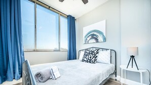Un dormitorio moderno con una cama grande, una lámpara de pie y vistas al cielo a través de una ventana.