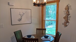 Un coin repas avec une table et des chaises en bois, un lustre, une carte encadrée et une fenêtre donnant sur des arbres.