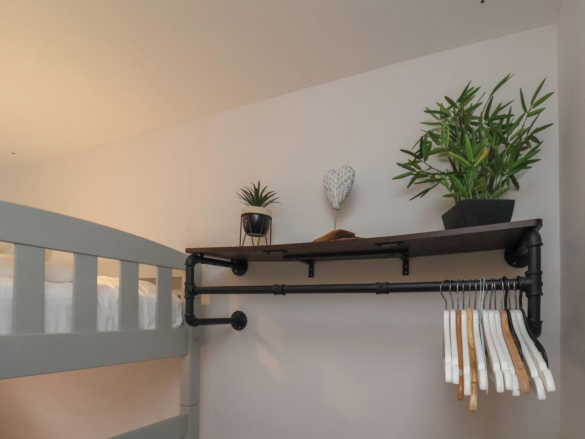 Uma escada com corrimão de metal, uma prateleira fixada na parede com plantas e objetos decorativos, e um cabideiro com ganchos brancos e castanhos.