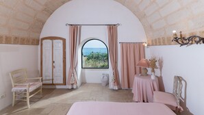Ein Schlafzimmer mit Meerblick, ein Holzstuhl, ein Bett, ein Tisch mit Lampe und ein dekoratives Wandbild.