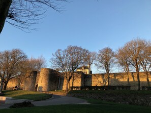A historic stone building with a central tower, surrounded by trees and a paved walkway.