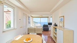 En moderne stue med en sofa, et spisebord med frugt, et fjernsyn og havudsigt.
