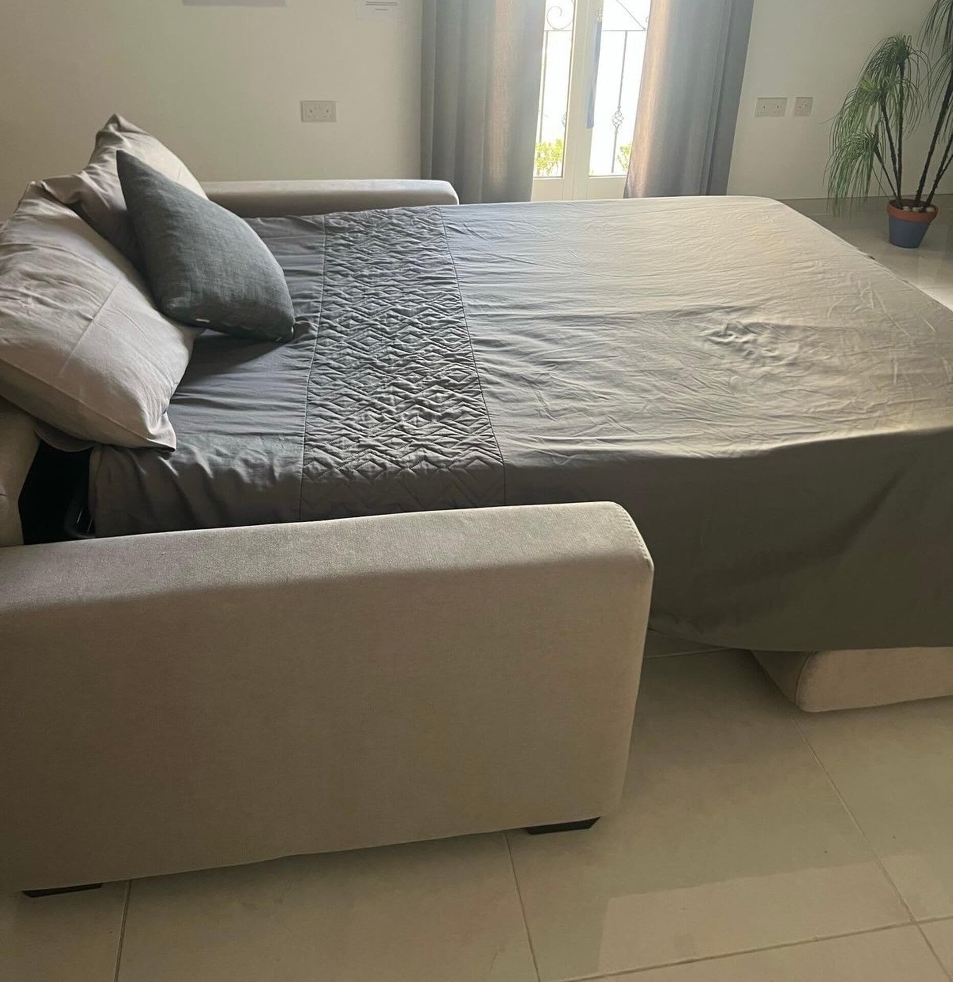 Ein modernes Schlafzimmer mit Bett, Sitzbank und Topfpflanze.