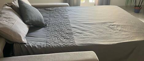 Ein modernes Schlafzimmer mit Bett, Sitzbank und Topfpflanze.