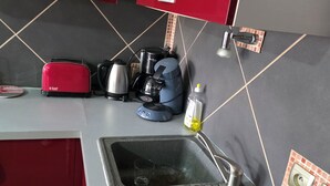 Ett kök med en diskho, en brödrost, en vattenkokare, en kaffebryggare och en flaska olja.