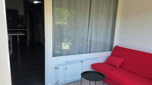 Ett rum med en röd soffa, ett litet svart bord, ett element och en utsikt genom ett fönster med gardiner.