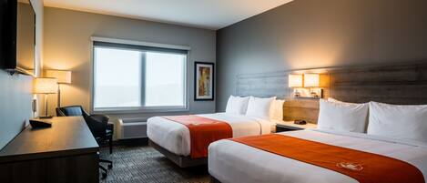 A hotel room with two beds, a desk, a chair, a window, and a wall-mounted TV.