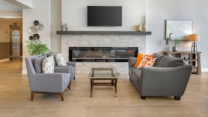 A modern living room with a fireplace, two sofas, a coffee table, and a flat-screen TV mounted above the fireplace. - Amsterdam Inn & Suites, an Ascend Collection Hotel (Florenceville-Bristol)
