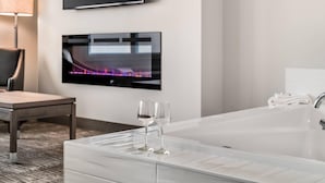 A modern bathroom with a large white bathtub, a flat-screen TV mounted on the wall, and a pair of wine glasses on the edge of the tub. - Amsterdam Inn & Suites, an Ascend Collection Hotel (Florenceville-Bristol)