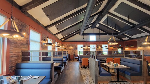 A restaurant interior with high ceilings, exposed beams, and a mix of blue and orange seating. - Amsterdam Inn & Suites, an Ascend Collection Hotel (Florenceville-Bristol)