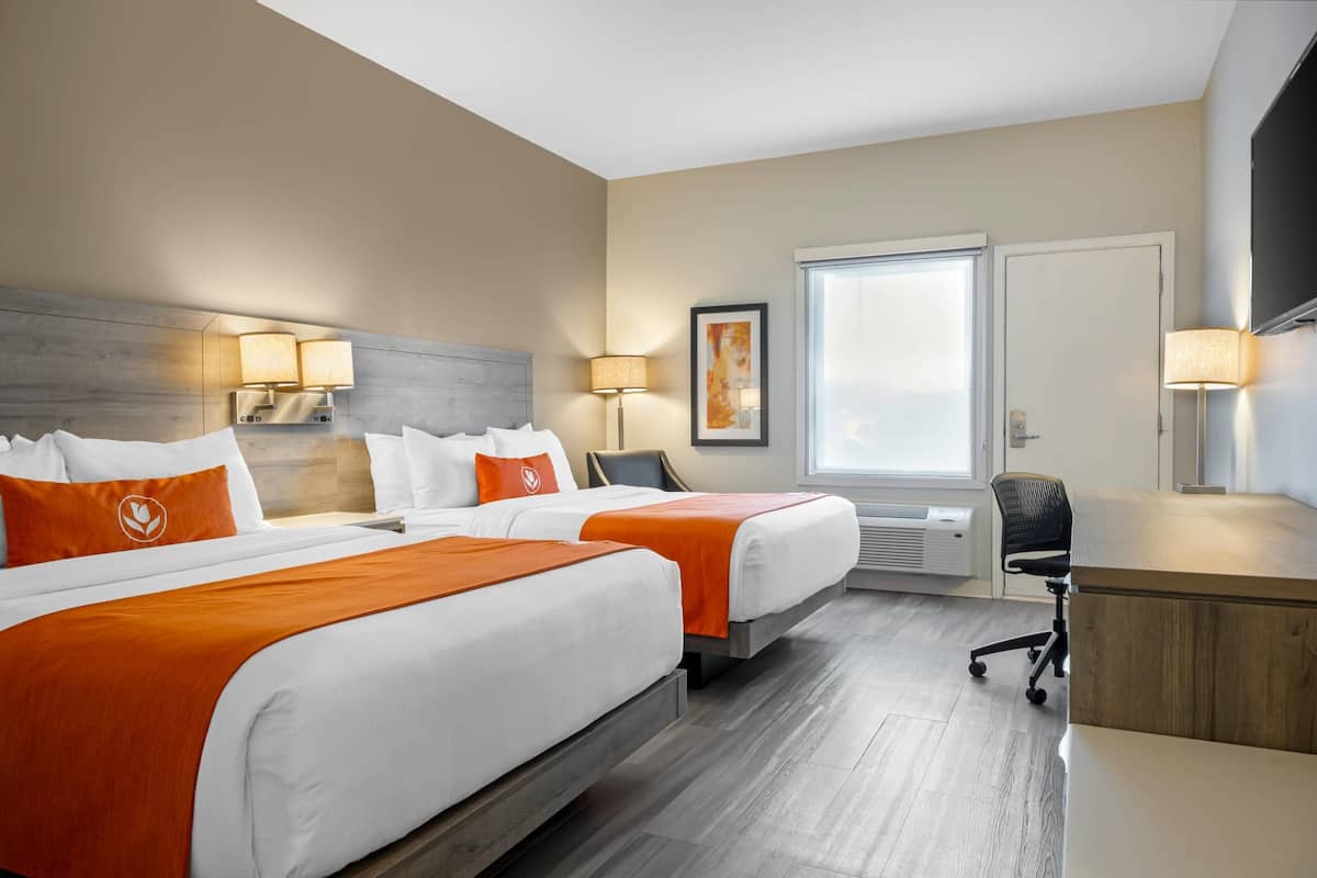 Een hotelkamer met twee bedden, een bureau en een stoel. Er is een raam met uitzicht, een lamp en een schilderij aan de muur.