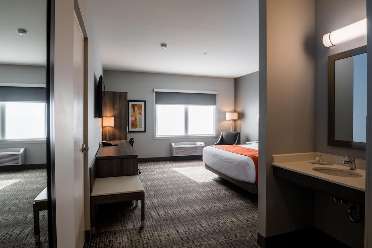 Een hotelkamer met een bed, bureau, stoel en een badkamer met wastafel en spiegel.