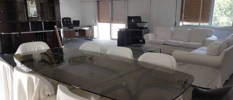 Uma sala de estar moderna com uma mesa de centro de vidro, sofás brancos, um armário de madeira escura e uma televisão.