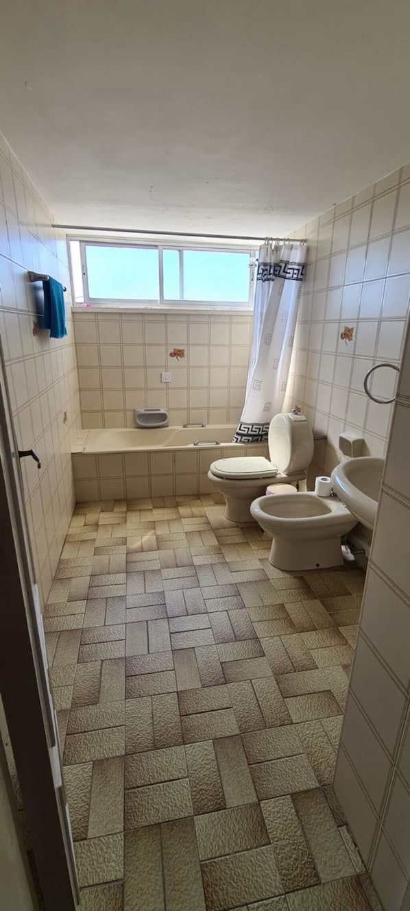A small bathroom with two toilets, a bathtub, and a window. - Large Student Penthouse in Nicosia · 4 Beds + Master En-Suite · Walk to Center (Nicosia)