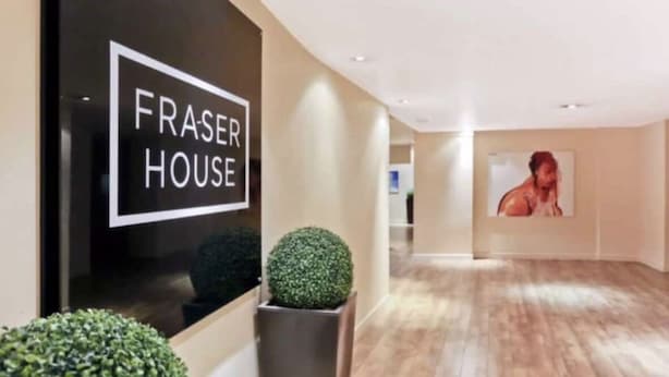 Un couloir avec une pancarte indiquant « FRASE HOUSE », une plante en pot et un grand tableau encadré accroché au mur.