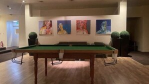 Une table de billard dans une pièce dont le sol est en bois et où sont accrochées quatre peintures au mur.